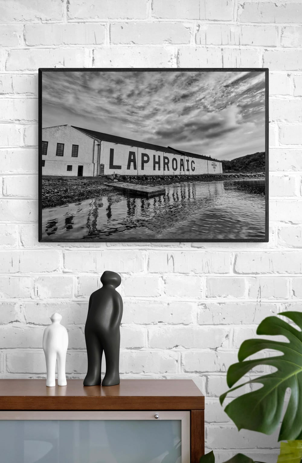 black and white statues looking up at a black and white framed photograph of laphroaig distillery warehouse with Laphroaig painted on side of building