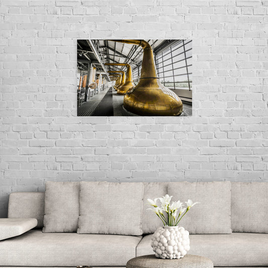colour photograph of copper stills at glen ord distillery. the background of the image has been desaturated to make the copper colour of the stills and condensors really stand out. the photo is on a light grey brick wall and above a wove light grey couch.  a white vase with white flowers is in the lower foreground